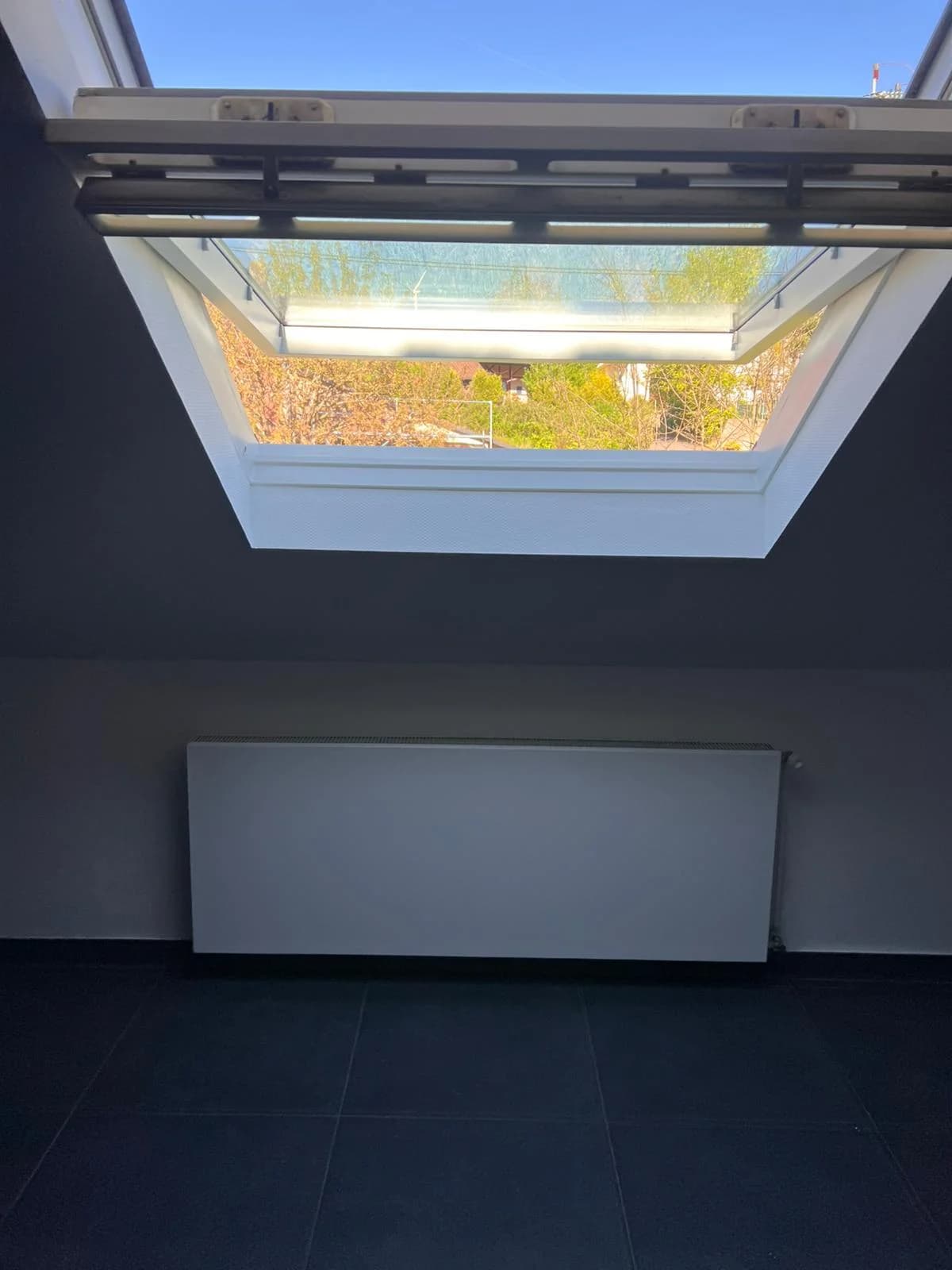 Weiß lackierter Fensterrahmen eines Dachfensters und weiß lackierter Plattenheizkörper unter der Dachschräge, Arbeit des Betriebs Siebert.